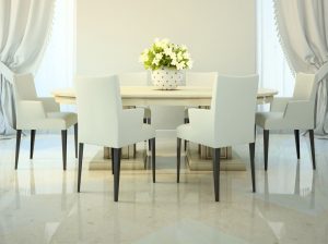 large oval stone dining room table with pedestal style legs and six white dining chairs with armrests